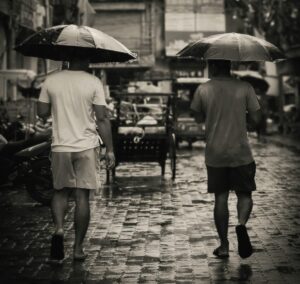 black and white photo of two men with their backs to the camera, they are wearing shorts and holding umbrellas