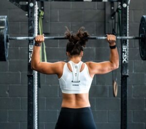 woman with her back to the camera lifting barbell, she is wearing a white vest and black leggings