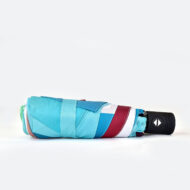 closed folding umbrella with black handle. Colourful print on the panels of the umbrella are shown closed